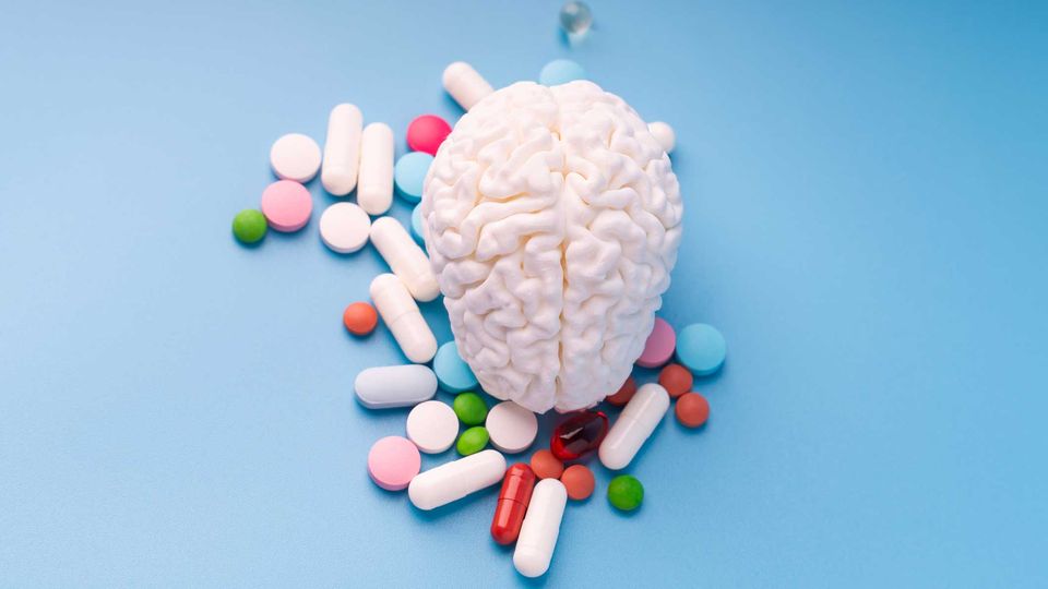 Birds-eye view of a brain model surrounded by an assortment of pills, on a blue surface.