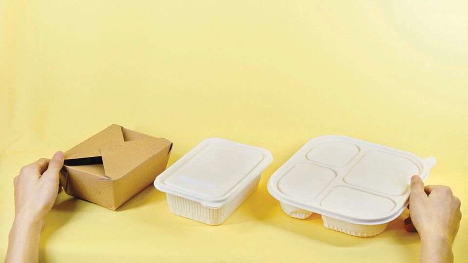 A person setting out a row of different food packaging boxes, made of cardboard and plastic.