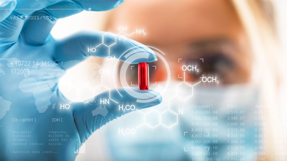 Close up image of female scientist holding a red pill in a blue gloved hand.