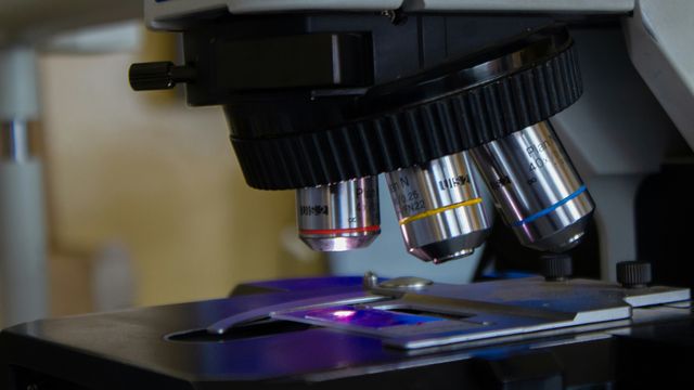 A close-up photograph of a microscope focusing a beam of light onto a glass sample slide. 