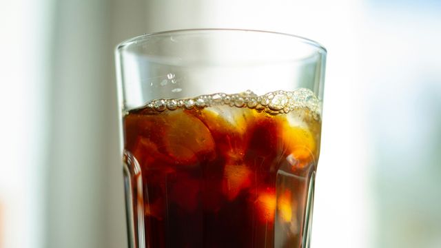 A tall glass containing ice cubes and cola. 