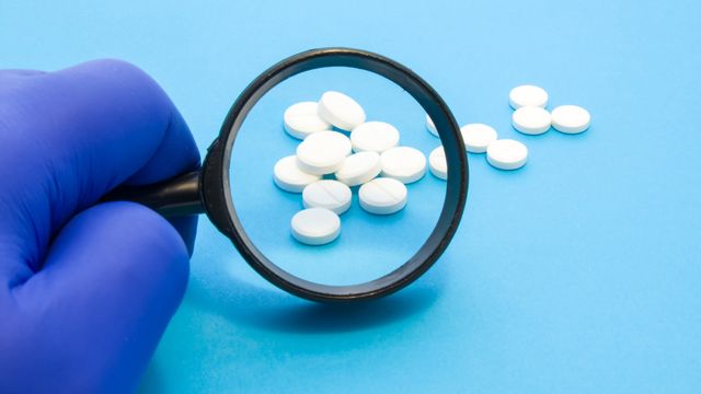 Magnifying glass looking over an assortment of white pills laid out on a blue surface. 