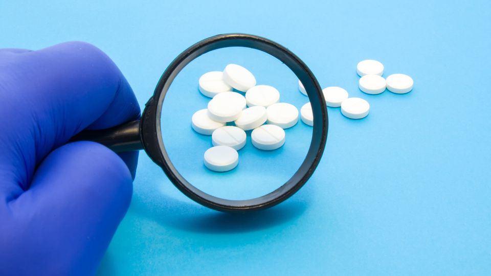 Magnifying glass looking over an assortment of white pills laid out on a blue surface.