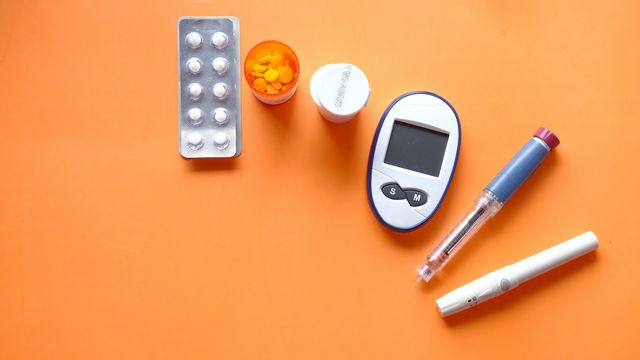 Blood glucose meter alongside pills, medicine bottles, and insulin pen supplies. 