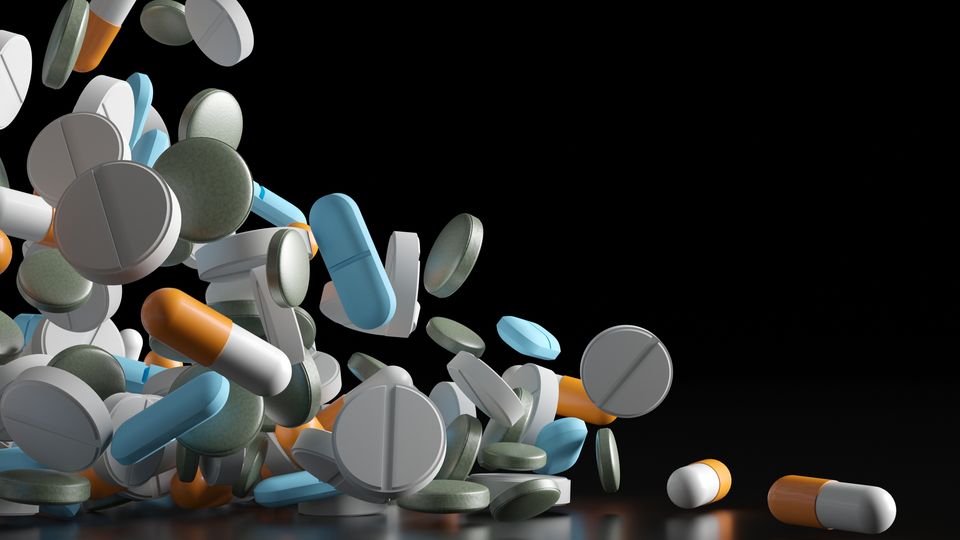 An assortment of pills falling to a flat surface against a black background.