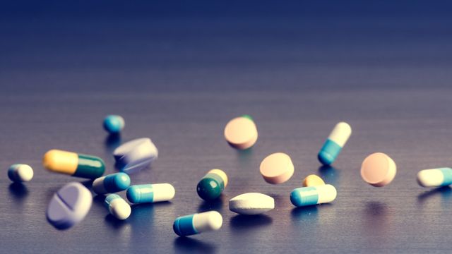 An assortment of pills and capsules appearing to fall onto a flat, gray surface. 