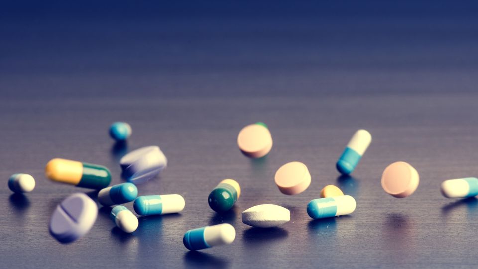 An assortment of pills and capsules appearing to fall onto a flat, gray surface.