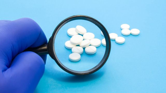 Magnifying glass looking over white pills laid out on a blue surface. 