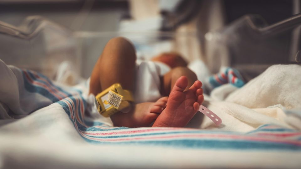 Preterm baby resting in a hospital bassinet with identification bands on the ankle.