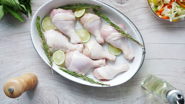 Raw chicken legs in a large baking dish, with slices of lemon and herbs. 