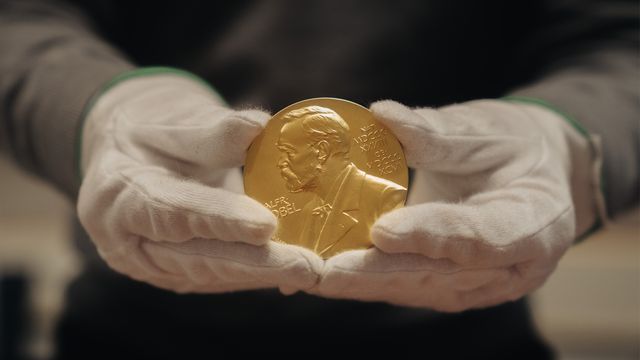 A gloved hand holding a gold Nobel Prize medal. 