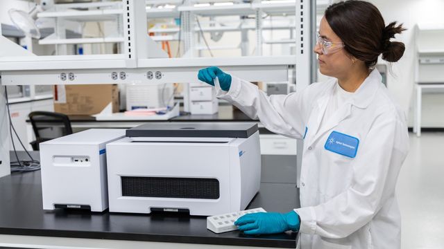 Researcher in a laboratory handling a sample near scientific equipment. 