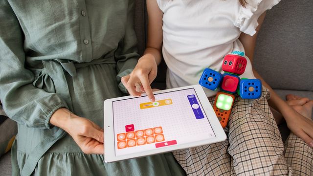 Child and adult using a tablet with coding blocks and interactive cubes during an autism learning activity. 