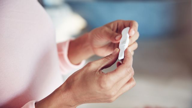 Hands holding a home pregnancy test near a rounded abdomen, representing pregnancy. 