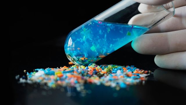 Small plastic fragments in front of a glass test tube, filled with clear blue liquid and more plastic fragments. 