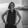 Woman researcher standing confidently by a waterfront with modern buildings in the background.