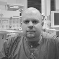 A black and white image of Dr. Junker, smiling at the camera. He is a bald man with a beard, wearing a light-colored button up shirt.