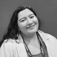 A black and white image of Aridjis-Olivos, smiling at the camera. She is a Hispanic woman with long black hair, wearing a white collared jacket and dark top.