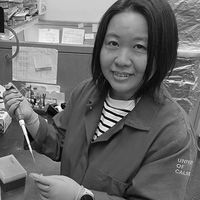 Smiling researcher in a laboratory coat using a pipette at a lab bench, engaged in scientific work.