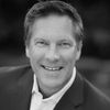 Professional black and white headshot of a smiling CEO in a suit jacket.