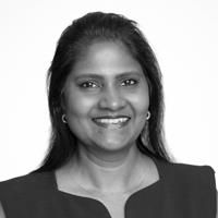 A black and white image of Venkat, smiling at the camera. She is an Indian woman wearing a dark-coloured dress.