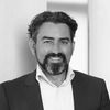 Professional black-and-white headshot of a smiling man in a suit with a beard and wavy hair.