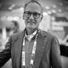 Black-and-white headshot of a man in glasses and a blazer wearing a conference lanyard.