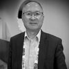 Black-and-white headshot of a man in glasses and a suit jacket wearing a conference lanyard.