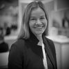 Black and white headshot of a smiling woman in professional attire at an indoor event.