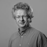 Black-and-white headshot of a smiling man with curly hair and glasses.