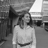 A black and white image of Mrhar. She is standing outside of a university building, smiling and looking off into the distance.