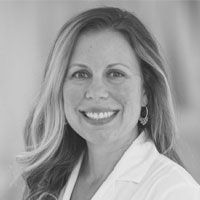 A grayscale image of Dr. Elizabeth Wellberg, wearing a lab coat and smiling at the camera.