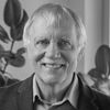 Black-and-white headshot of a person in a blazer, facing the camera with indoor plants in the background.
