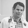 A black and white image of Richards, smiling at the camera. He is wearing a lab coat and a stethoscope.